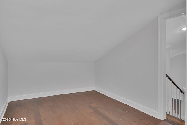 additional living space featuring dark wood-type flooring, vaulted ceiling, and baseboards