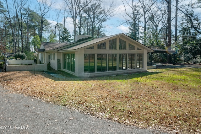 view of side of property with a yard, a sunroom, a chimney, and brick siding