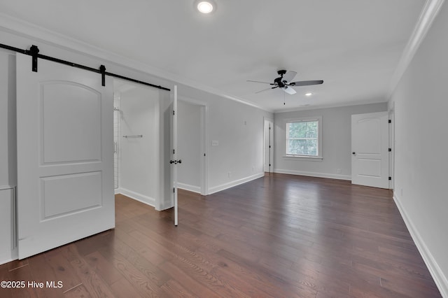 interior space featuring a barn door, baseboards, a ceiling fan, ornamental molding, and dark wood-style flooring