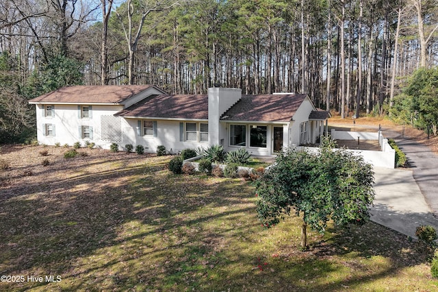 ranch-style house featuring driveway, a chimney, and a front lawn