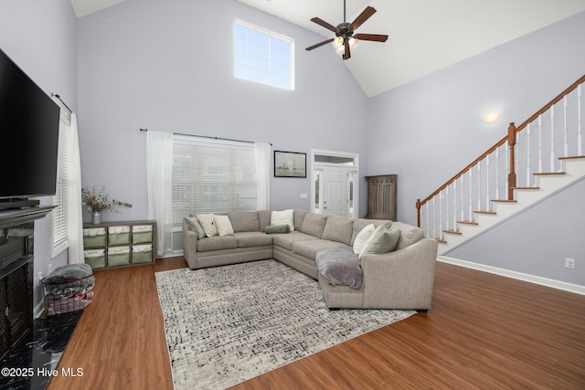 living area with dark wood-type flooring, a ceiling fan, high vaulted ceiling, and stairs