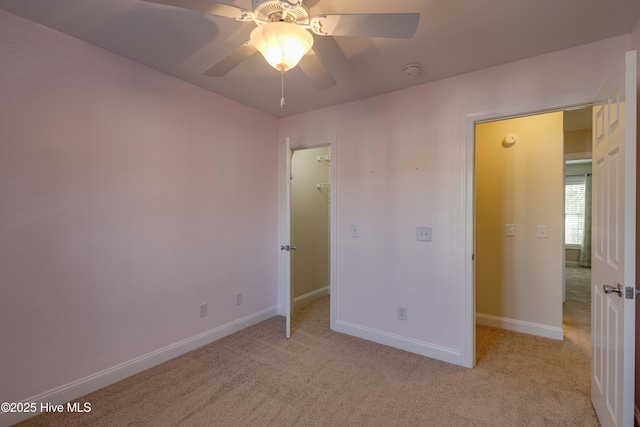 unfurnished bedroom with light carpet, a spacious closet, and ceiling fan