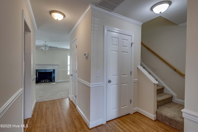 hallway with crown molding, light hardwood / wood-style flooring, and a textured ceiling