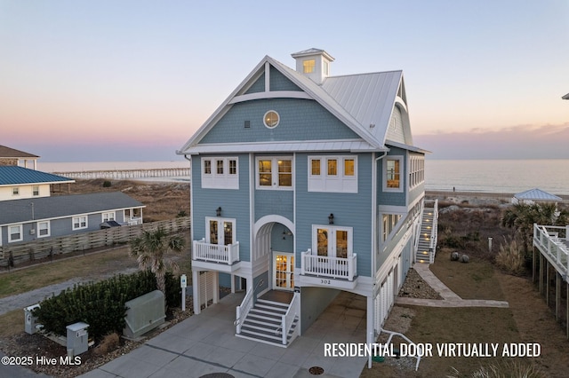 raised beach house with stairway, french doors, metal roof, driveway, and a standing seam roof