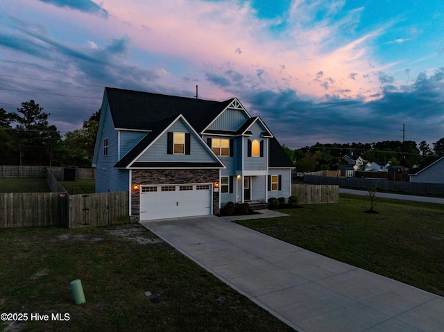 view of front of house featuring concrete driveway, stone siding, an attached garage, fence, and a yard
