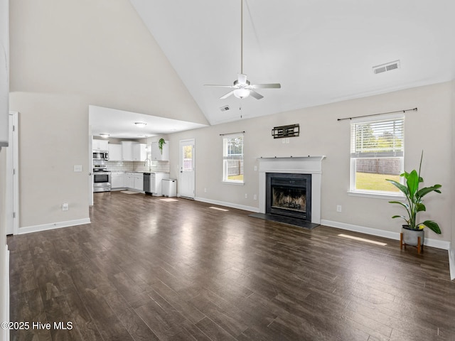 unfurnished living room featuring a fireplace with raised hearth, visible vents, a ceiling fan, a healthy amount of sunlight, and dark wood-type flooring