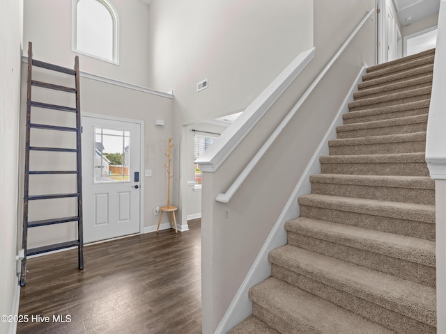 entryway with a high ceiling, wood finished floors, stairs, and visible vents