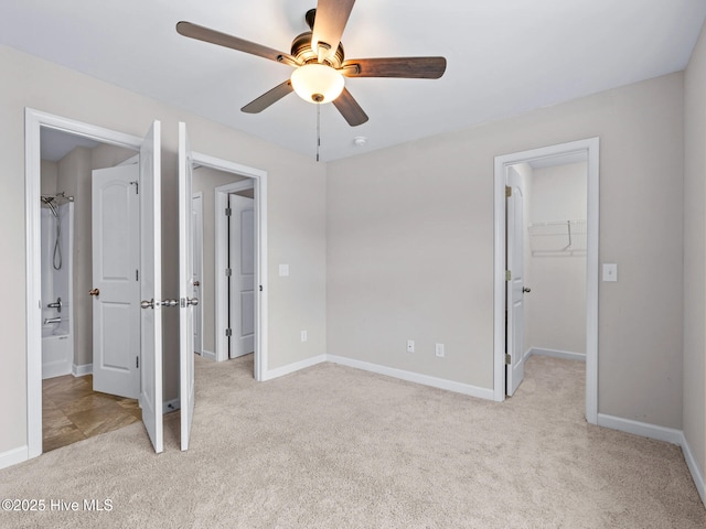 unfurnished bedroom with light carpet, a walk in closet, a closet, baseboards, and ceiling fan