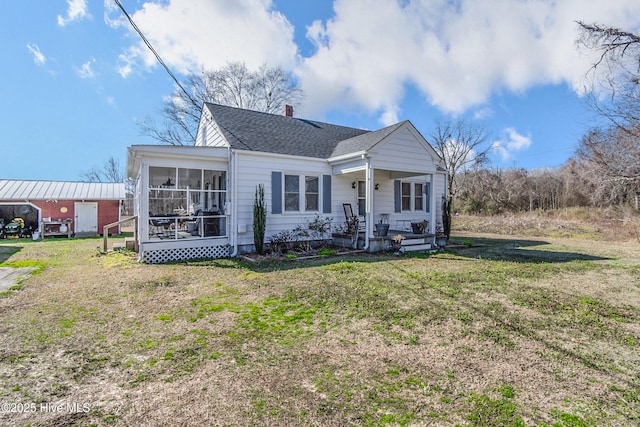 bungalow featuring a chimney, roof with shingles, a front lawn, and a sunroom