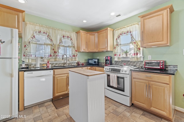 kitchen featuring light brown cabinetry, white appliances, stone tile flooring, and a sink