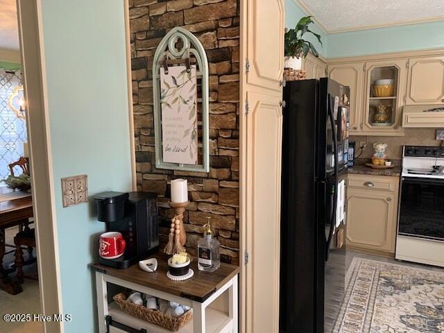 kitchen with electric range oven, range hood, cream cabinets, a textured ceiling, and black fridge