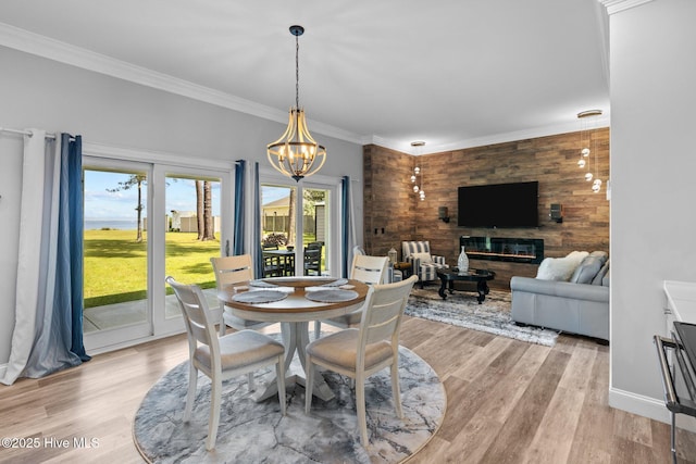 dining space with a chandelier, a glass covered fireplace, ornamental molding, and light wood-style flooring