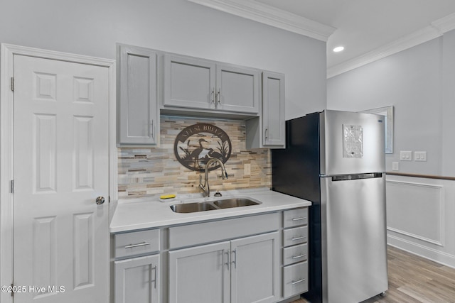 kitchen featuring freestanding refrigerator, light countertops, crown molding, gray cabinetry, and a sink