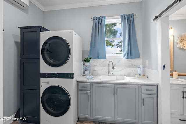 clothes washing area featuring a barn door, a sink, an AC wall unit, stacked washing maching and dryer, and cabinet space