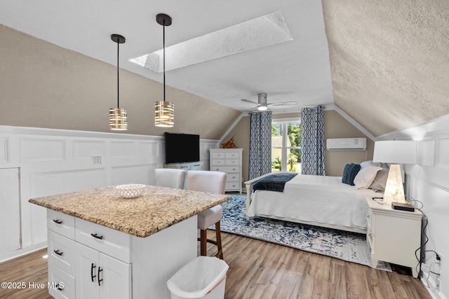 bedroom featuring a textured ceiling, lofted ceiling with skylight, a wall unit AC, and wood finished floors