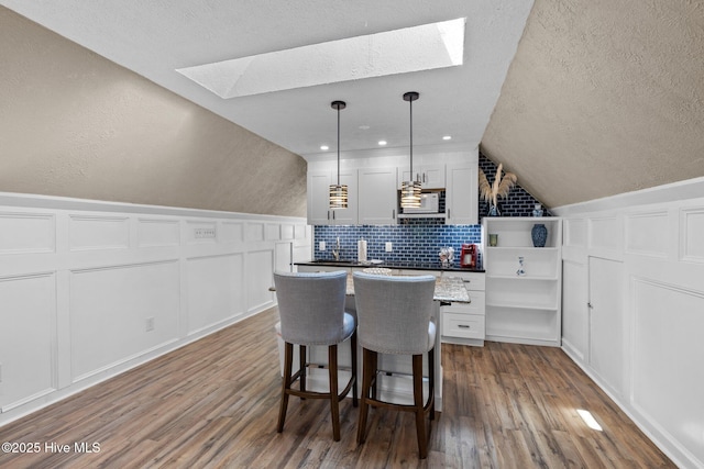 kitchen with open shelves, hanging light fixtures, white microwave, lofted ceiling with skylight, and white cabinets