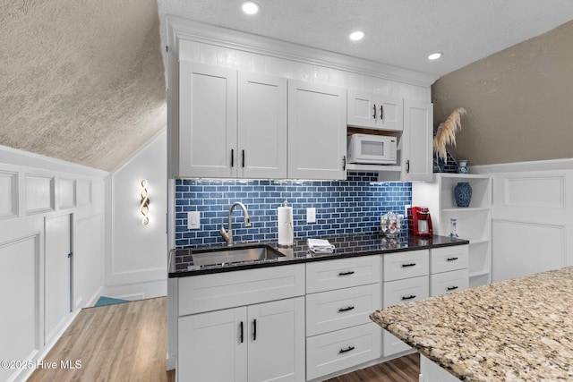 kitchen featuring light stone countertops, white cabinets, a sink, and white microwave