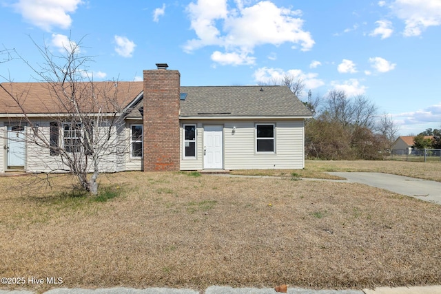 back of property with a shingled roof, a lawn, and a chimney