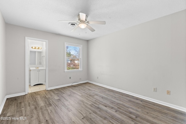 unfurnished bedroom featuring connected bathroom, wood finished floors, baseboards, and a textured ceiling