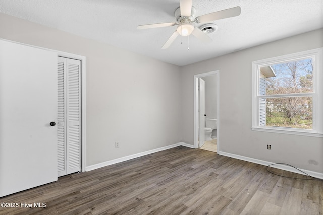 unfurnished bedroom with baseboards, ensuite bath, wood finished floors, a closet, and a textured ceiling