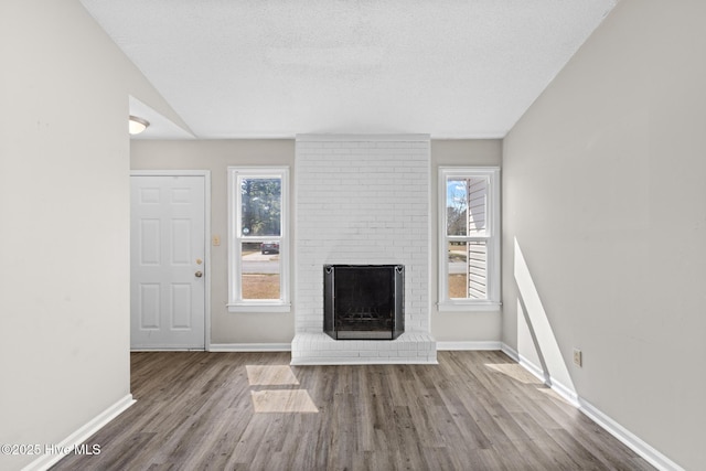 unfurnished living room with a brick fireplace, baseboards, and wood finished floors