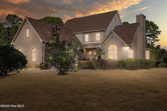 view of front of property with a yard, roof with shingles, a chimney, and brick siding