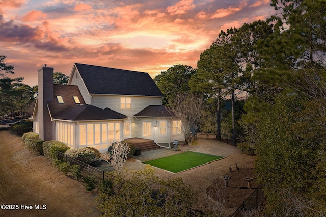 back of house at dusk featuring a patio area, fence, and a chimney