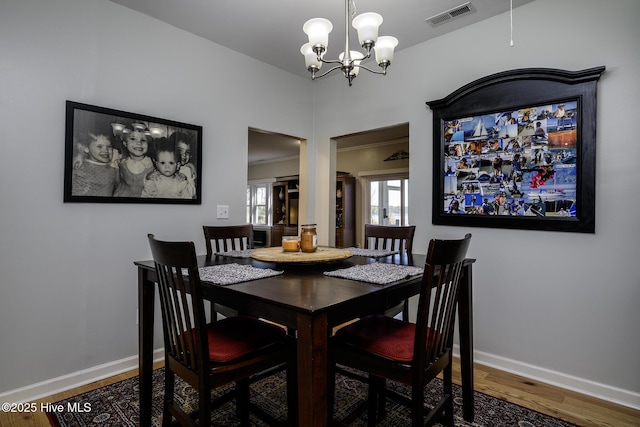 dining area featuring baseboards, visible vents, a chandelier, and wood finished floors