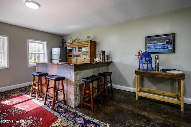 bar featuring a bar, baseboards, and freestanding refrigerator