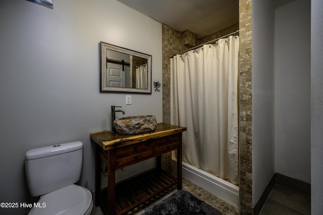 bathroom with a stall shower, baseboards, a sink, and toilet