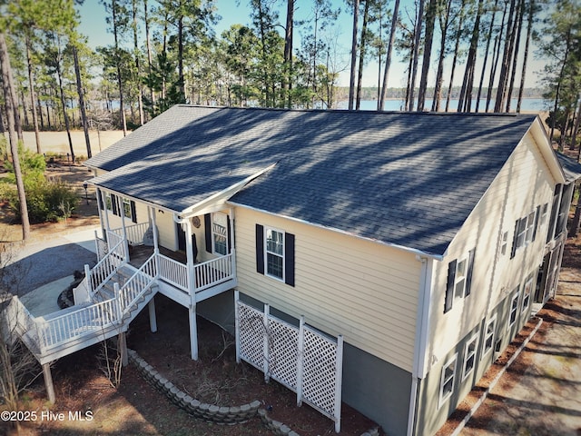 view of side of home featuring covered porch, stairway, and roof with shingles