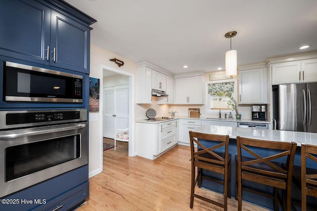 kitchen with stainless steel appliances, light countertops, light wood-style floors, a sink, and under cabinet range hood