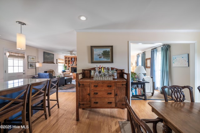 dining room with ceiling fan, recessed lighting, light wood-type flooring, a brick fireplace, and crown molding