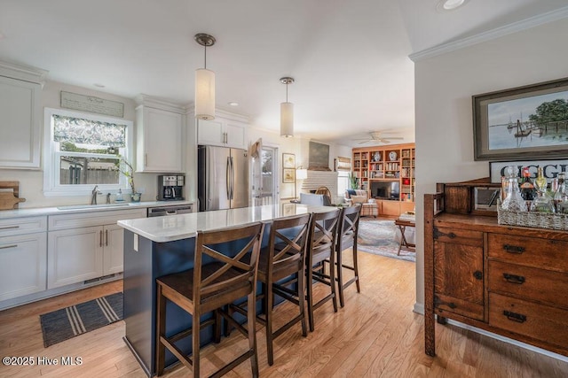 kitchen with a breakfast bar, light wood-style flooring, appliances with stainless steel finishes, a brick fireplace, and a sink