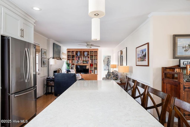 dining space featuring ornamental molding, a ceiling fan, a brick fireplace, and wood finished floors