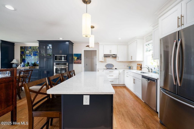 kitchen featuring appliances with stainless steel finishes, light wood-style floors, a sink, under cabinet range hood, and a kitchen bar