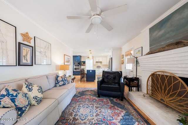 living area with light wood-style floors, a brick fireplace, a ceiling fan, and crown molding