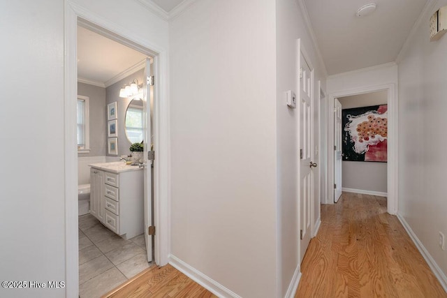 hallway featuring a sink, light wood-style flooring, baseboards, and crown molding