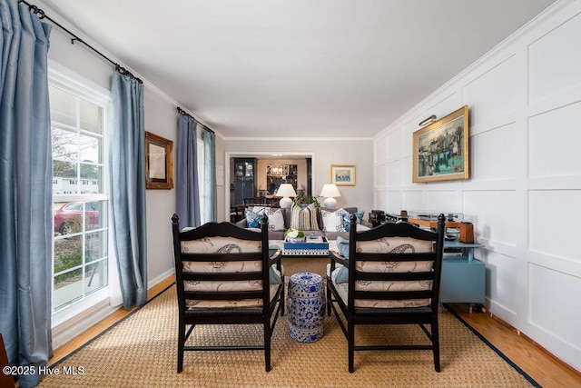 dining area featuring ornamental molding, light wood-style flooring, and a decorative wall