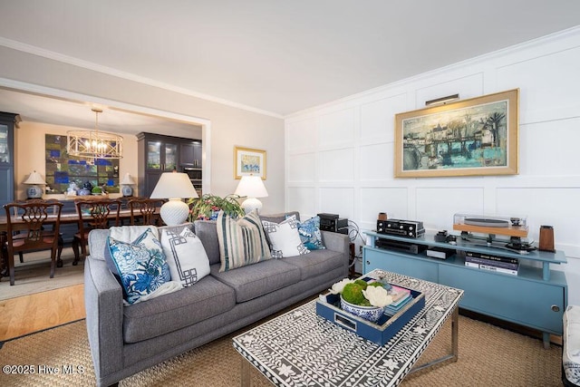 living area featuring crown molding, a notable chandelier, light wood-style flooring, and a decorative wall