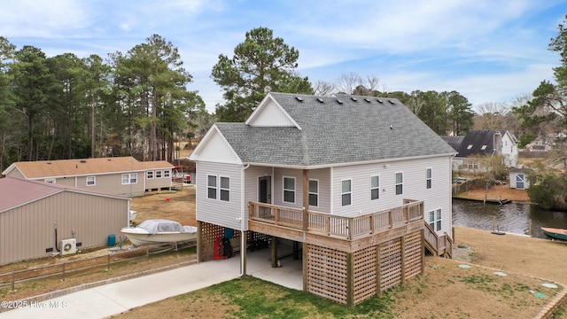 rear view of property with a deck with water view, a carport, concrete driveway, and a shingled roof