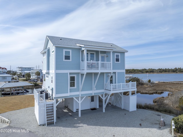 raised beach house with a balcony, a shingled roof, a water view, driveway, and a carport