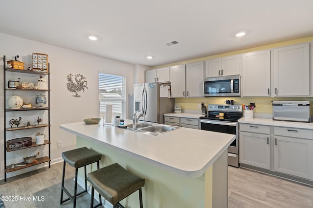 kitchen with sink, a breakfast bar area, light hardwood / wood-style flooring, appliances with stainless steel finishes, and a kitchen island with sink