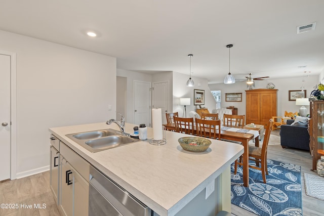 kitchen with dishwasher, sink, hanging light fixtures, a kitchen island with sink, and light hardwood / wood-style flooring