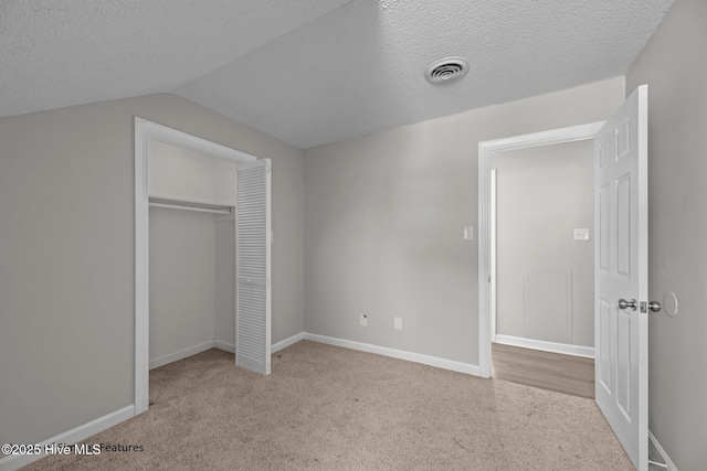 unfurnished bedroom featuring light carpet, a closet, vaulted ceiling, and a textured ceiling