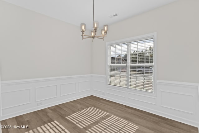 empty room with a chandelier, wainscoting, dark wood-style floors, and visible vents