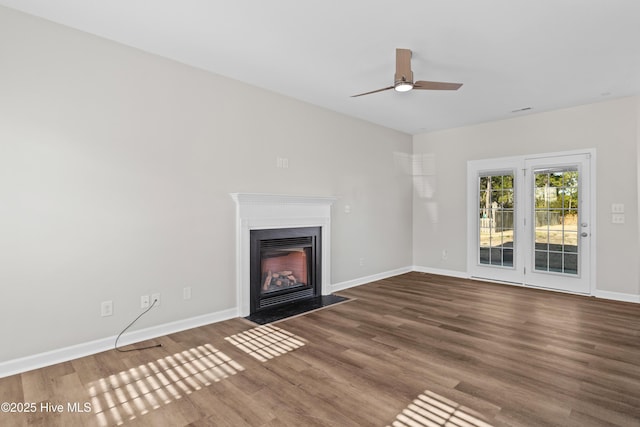 unfurnished living room with a fireplace with flush hearth, ceiling fan, baseboards, and wood finished floors