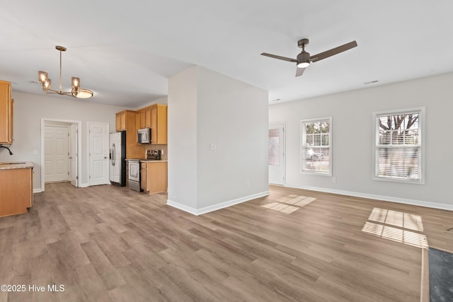 unfurnished living room with visible vents, baseboards, light wood-type flooring, a sink, and ceiling fan with notable chandelier