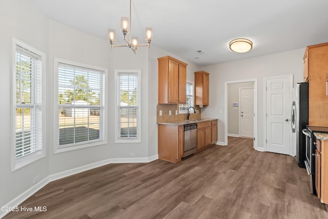 kitchen featuring stainless steel appliances, a sink, baseboards, light stone countertops, and dark wood-style floors