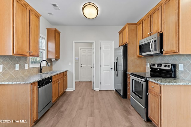 kitchen with light stone counters, light wood-style flooring, stainless steel appliances, a sink, and baseboards